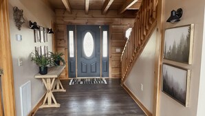 A wooden interior hallway with a dark wooden floor, a wooden staircase on the right, and a door with a decorative glass panel at the end.