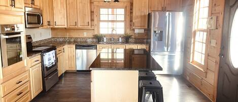 A kitchen with wooden cabinets, stainless steel appliances, a granite countertop, and a large window.