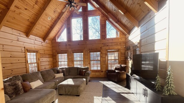A log cabin interior with a large L-shaped sectional sofa, a recliner, a flat-screen TV, and a fireplace.