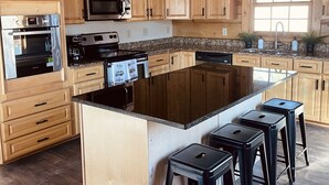 A spacious kitchen with wooden cabinets, a large island with bar stools, stainless steel appliances, and a window providing natural light.