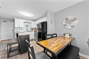Enjoy meals in the kitchen and dining area with a clean, minimalist design featuring a refrigerator, stainless steel appliances, and a wooden table.