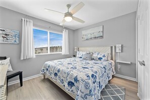 Relax in this serene bedroom with a large bed, nightstand, and bench, surrounded by wall art and natural light.