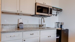 A kitchen with white cabinets, a stainless steel microwave, a coffee machine, and a sink. - Unit 22 Waena Inn - Maui Private Suite (Wailuku)