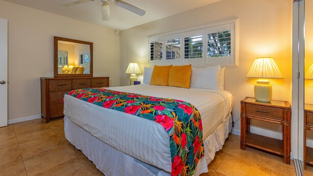 A hotel room with a bed, a ceiling fan, a window with blinds, a dresser, and two bedside lamps. - Kihei Beach, #107 1 Bedroom Condo by RedAwning (Kihei)