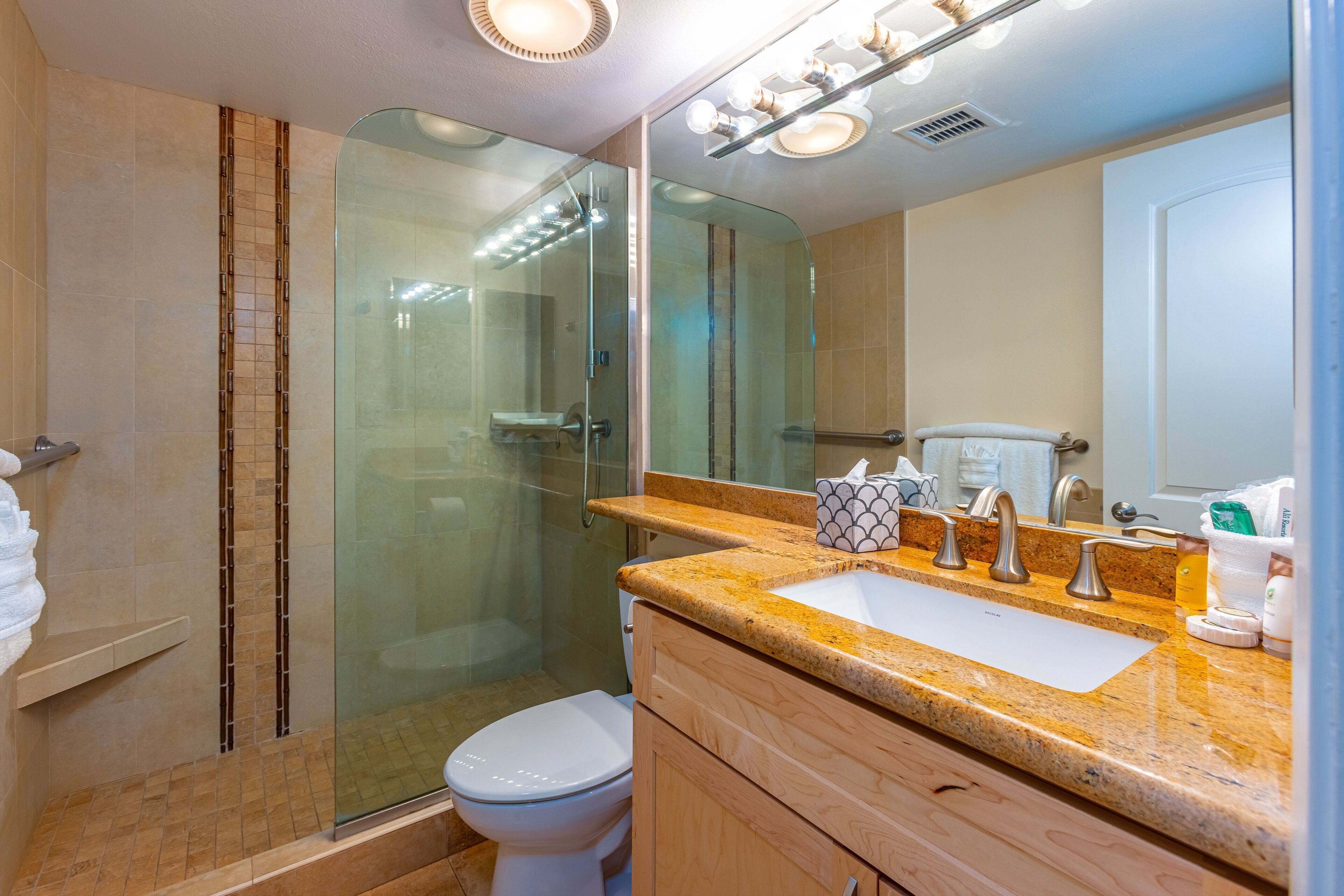 Une salle de bain moderne avec une douche à parois de verre, des toilettes blanches, un meuble-lavabo et un miroir avec des lumières au-dessus.