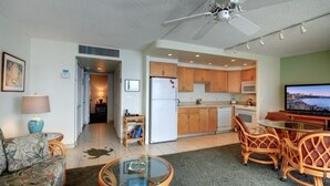 A living room with a sofa, a glass coffee table, a TV, and a dining area with chairs. - Kihei Beach, #405 1 Bedroom Condo by RedAwning (Kihei)