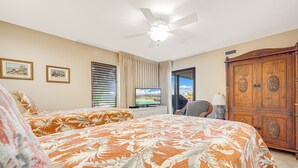 Ein Hotelzimmer mit zwei Betten, einem Deckenventilator, einem Fernseher und einem großen Holzschrank.