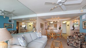 A living room with a sofa, chairs, a coffee table, a ceiling fan, and a kitchen area in the background. - Kihei Beach, #509 2 Bedroom Condo by RedAwning (Kihei)