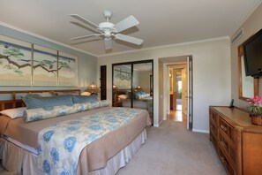 A hotel room with a bed, a ceiling fan, a television, and a mirror.