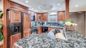 A kitchen with wooden cabinets, granite countertops, a coffee maker, and a ceiling fan.