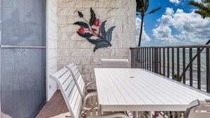 A balcony with a white table and chairs, a decorative wall art, and a view of the ocean. - Kihei Beach, #409 2 Bedroom Condo by RedAwning (Kihei)