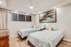 Un dormitorio con dos camas, un ventilador de techo, un cuadro y una ventana con cortinas.