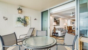 A dining area with a glass table and chairs, a painting on the wall, and a sliding glass door leading to a living room. - Royal Mauian, #517 2 Bedroom Condo by RedAwning (Kihei)