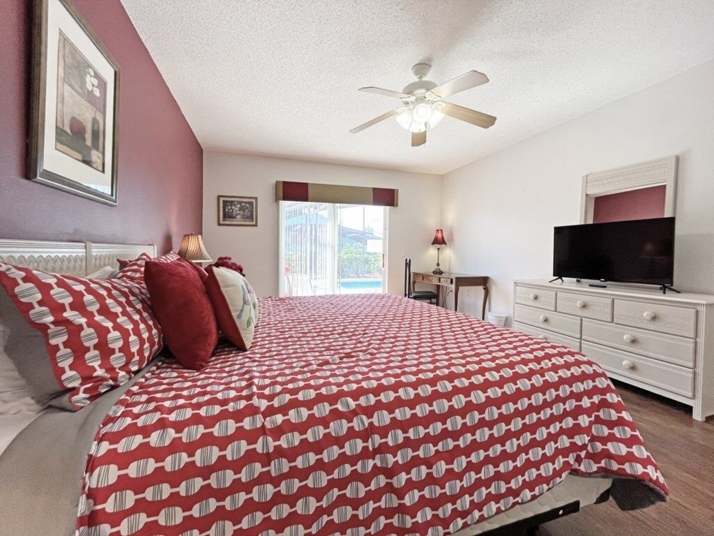 A bedroom with a bed, a television, a desk, and a ceiling fan.