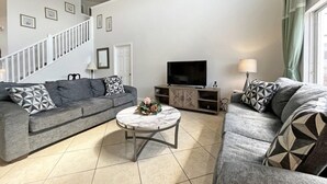 Ein Wohnzimmer mit zwei grauen Sofas, einem runden Couchtisch, einem Flachbildfernseher und einer Treppe.