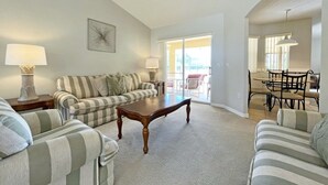 A spacious living room with striped sofas, a wooden coffee table, and a dining area with a table and chairs.