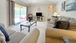 A living room with a sofa, a coffee table, a TV stand, and a ceiling fan.