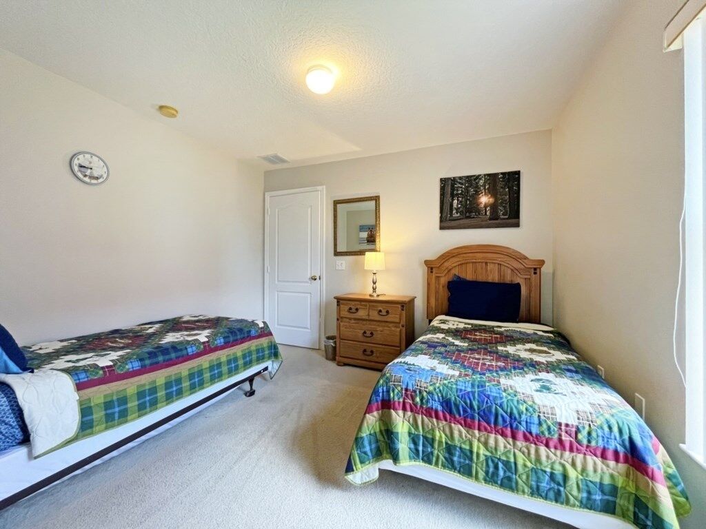 A bedroom with two single beds, a wooden dresser, a mirror, and a clock on the wall.