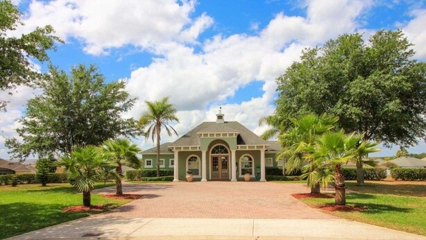 A two-story house with a central entrance, surrounded by a paved driveway and palm trees.