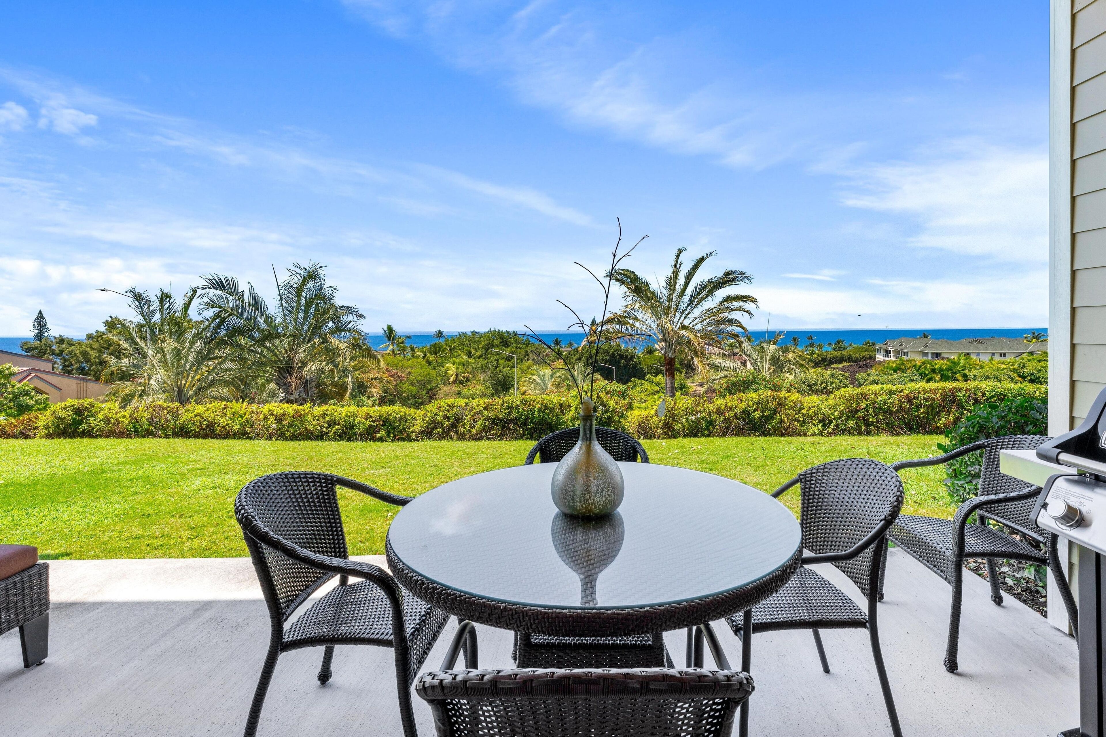 A patio with a round table and chairs, a vase, and a grill.