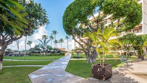 A well-maintained hotel courtyard with a paved walkway, lush greenery, and a large tree. - Sugar Beach Resort, #418 1 Bedroom Condo by RedAwning (Kihei)