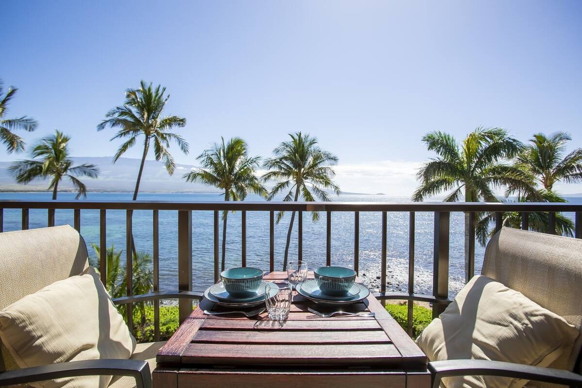 Ein Tisch mit Tellern und Gläsern auf einem Balkon mit Blick auf den Ozean und Palmen.