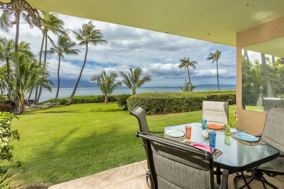 Eine Terrasse mit Tisch und Stühlen mit Blick auf eine üppige Rasenfläche und eine malerische Meerlandschaft.