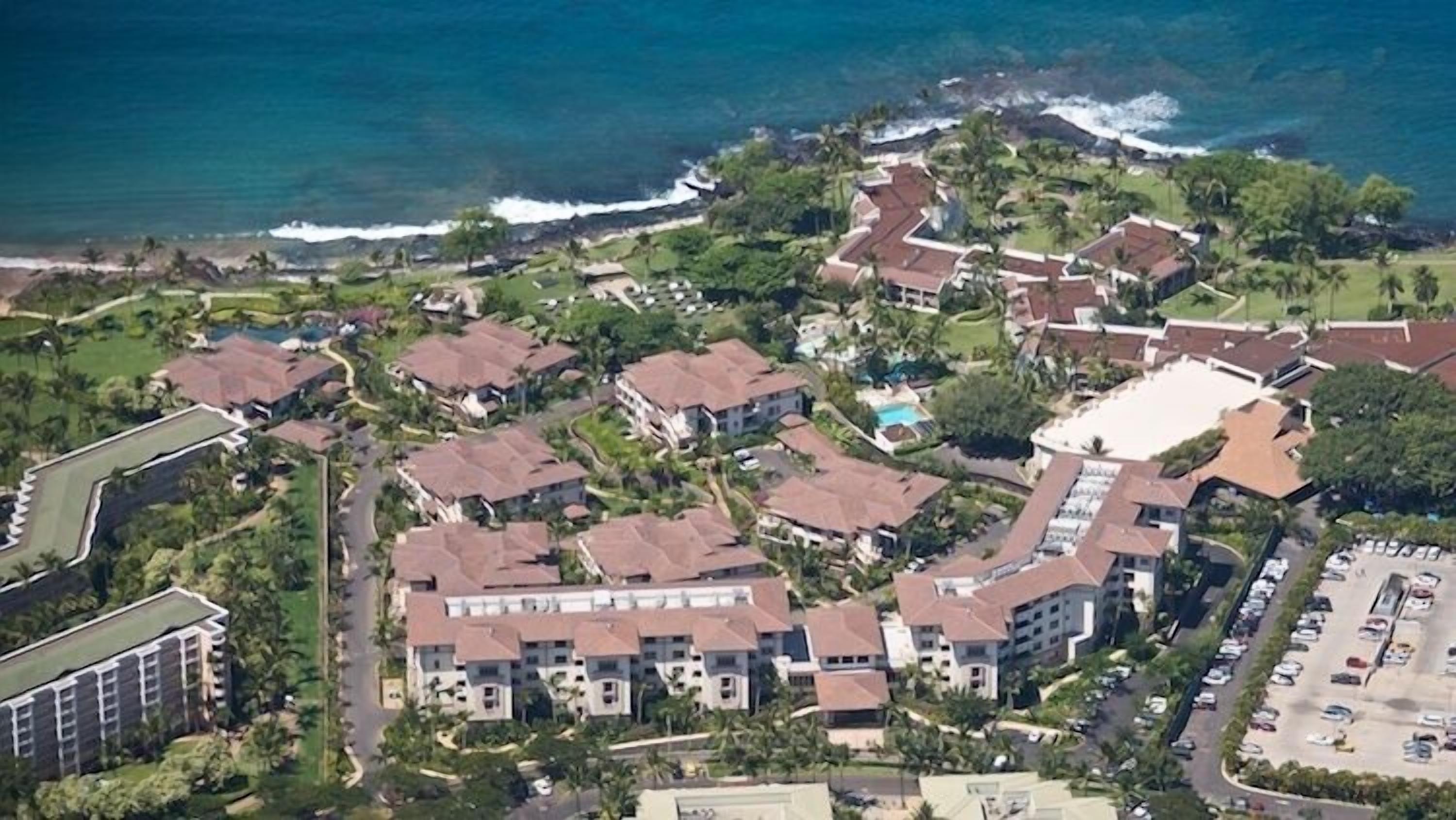 An aerial view of a coastal residential area with multiple buildings, including a large hotel with a swimming pool.
