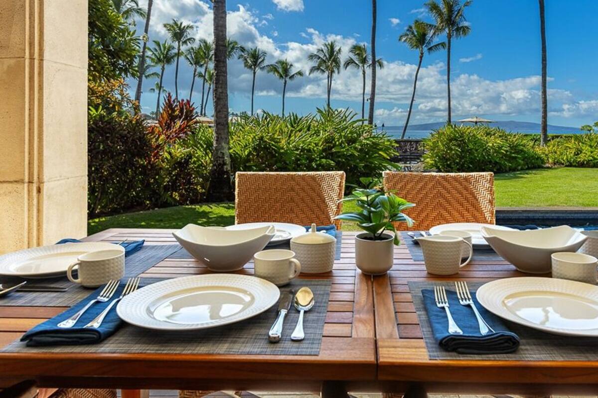 A dining table set for four with a view of palm trees and the ocean.