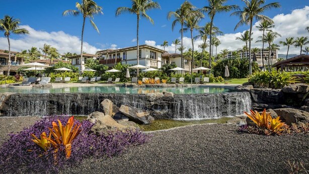 Ein Resort-Pool mit Wasserfall, umgeben von Palmen und Liegestühlen.