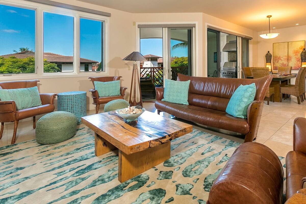 A spacious living room with a brown leather sofa, wooden coffee table, and green patterned rug.