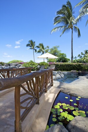 A wooden deck with a pool, palm trees, and a lounge area with an umbrella.