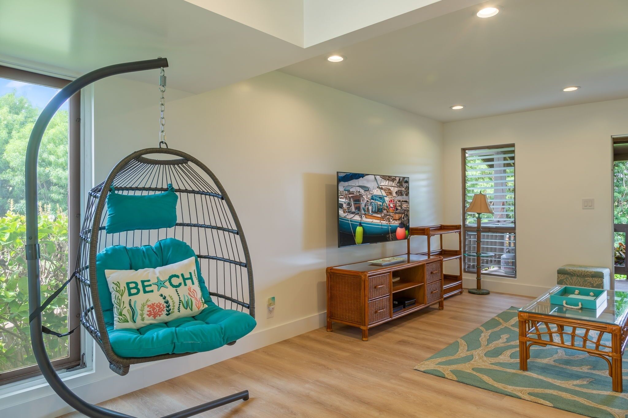 A modern living room with a hanging chair, a flat-screen TV, a wooden coffee table, and a view of greenery outside.