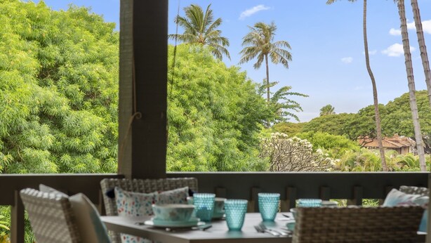 A covered outdoor seating area with wicker furniture and teal glassware, overlooking lush greenery and palm trees. - Kaanapali Plantation by Coldwell Banker Island Vacations (Lahaina)
