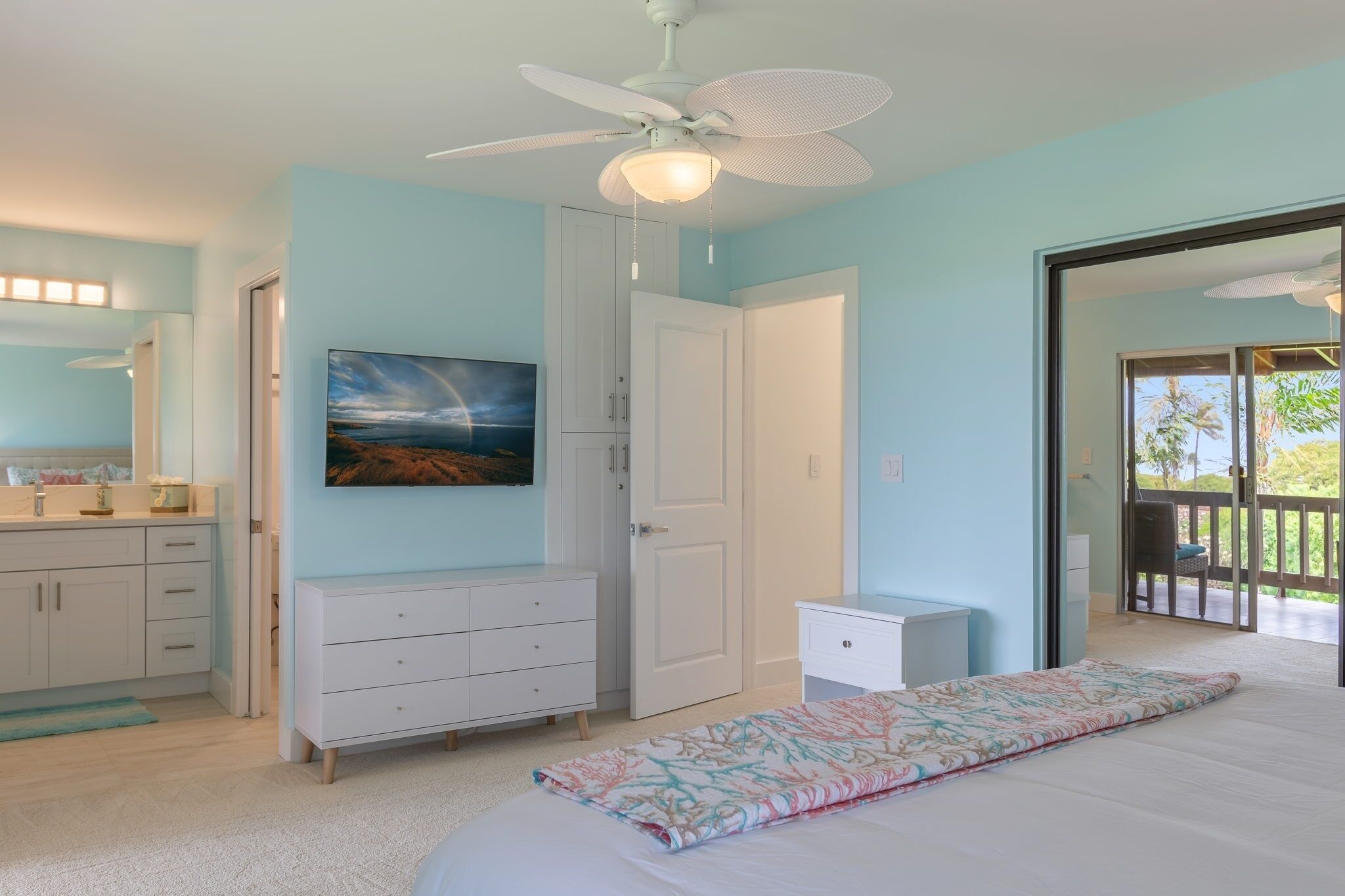 Une chambre à coucher comprenant un lit, un ventilateur de plafond, un tableau, une armoire et une porte donnant sur un balcon.