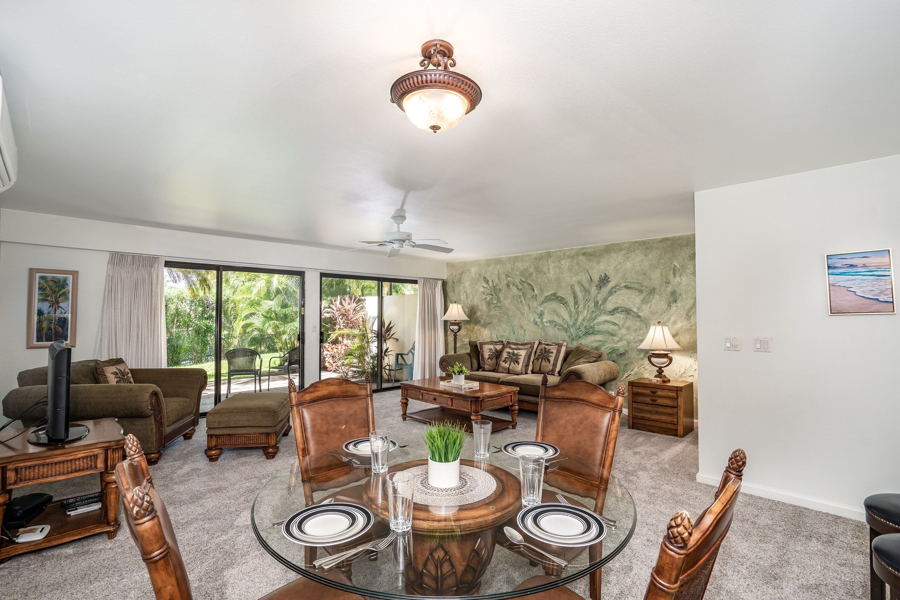 A spacious living room with a dining area, large windows, and a ceiling fan.
