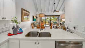 A kitchen with white cabinets, a double sink, and a dining area with wooden furniture. - Maui Kamaole by Coldwell Banker Island Vacations (Kihei)