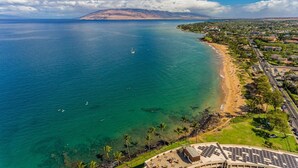An aerial view of a coastal area with a beach, clear blue waters, and a distant mountain range. - Maui Kamaole by Coldwell Banker Island Vacations (Kihei)