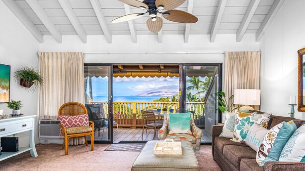 A cozy living room with a large window overlooking a scenic ocean view. There is a comfortable seating area with a sofa and chairs, a small table with a tray, and a decorative plant. - Maui Kamaole by Coldwell Banker Island Vacations (Kihei)