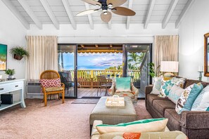 A cozy living room with a large window overlooking a scenic ocean view. There is a comfortable seating area with a sofa and chairs, a small table with a tray, and a decorative plant. - Maui Kamaole by Coldwell Banker Island Vacations (Kihei)