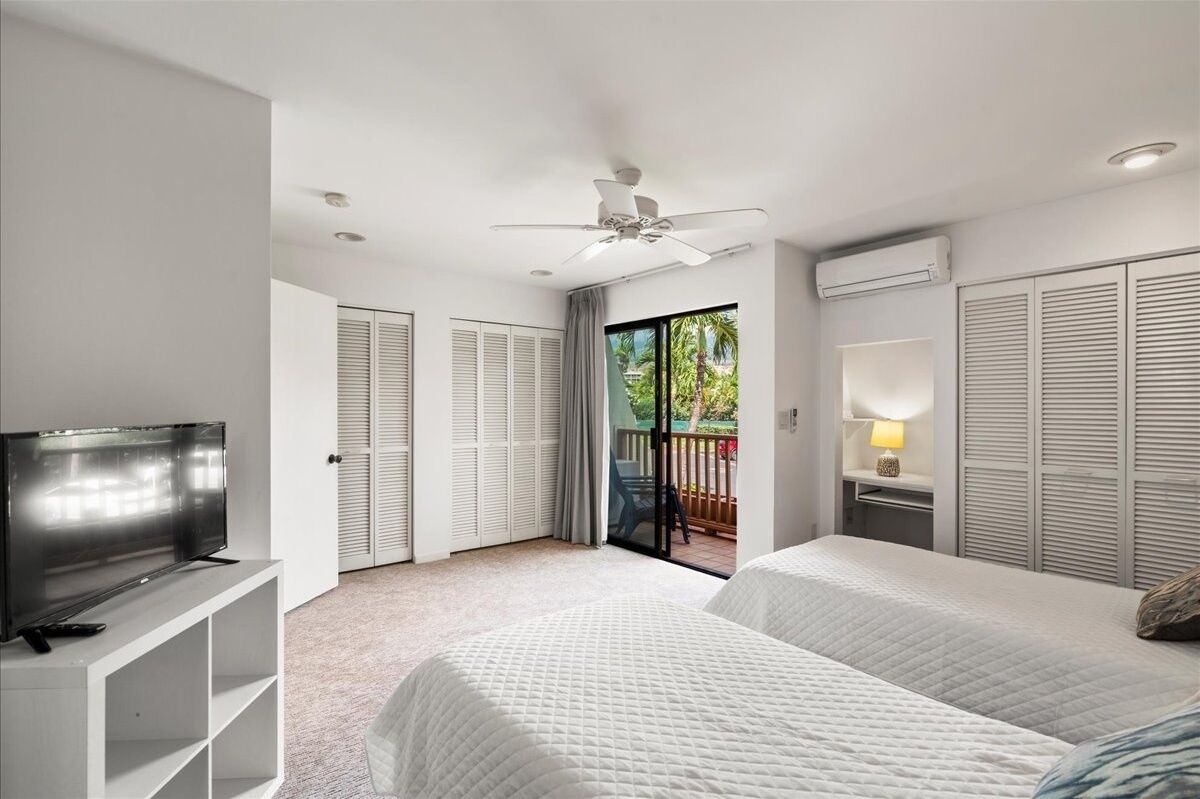 Habitación de hotel con cama, televisor, ventilador de techo y balcón con vistas a zonas verdes.