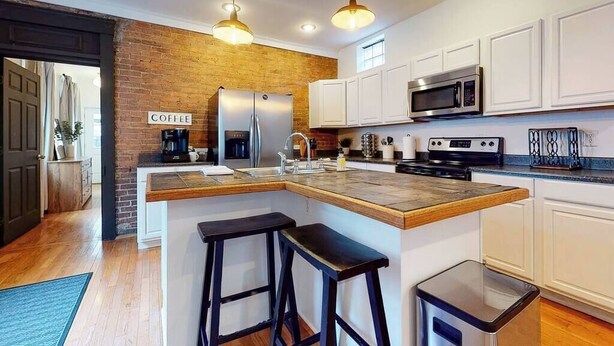 Una cocina moderna con una isla central, armarios blancos, pared decorativa de ladrillo y un letrero de café.
