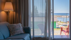 A room with a sofa, a lamp, and a view of the beach through a glass door. - Navigateur Ste-Luce (Sainte-Luce)