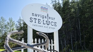 A sign with the text "navigateur STE. LUCÉ cabins sur plage" and a white fence in the background. - Navigateur Ste-Luce (Sainte-Luce)