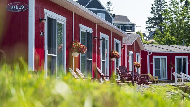 A row of red buildings with numbered doors, outdoor seating, and hanging flower baskets. - Navigateur Ste-Luce (Sainte-Luce)