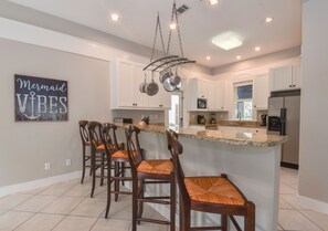 Una cocina moderna con armarios blancos, encimera de granito y un colgador para ollas.