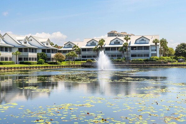 A hotel with a large pond and a fountain, surrounded by manicured lawns and palm trees.