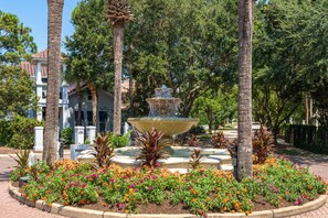 Un espace paysager agrémenté d’une fontaine centrale, entouré de plantes fleuries et de palmiers.