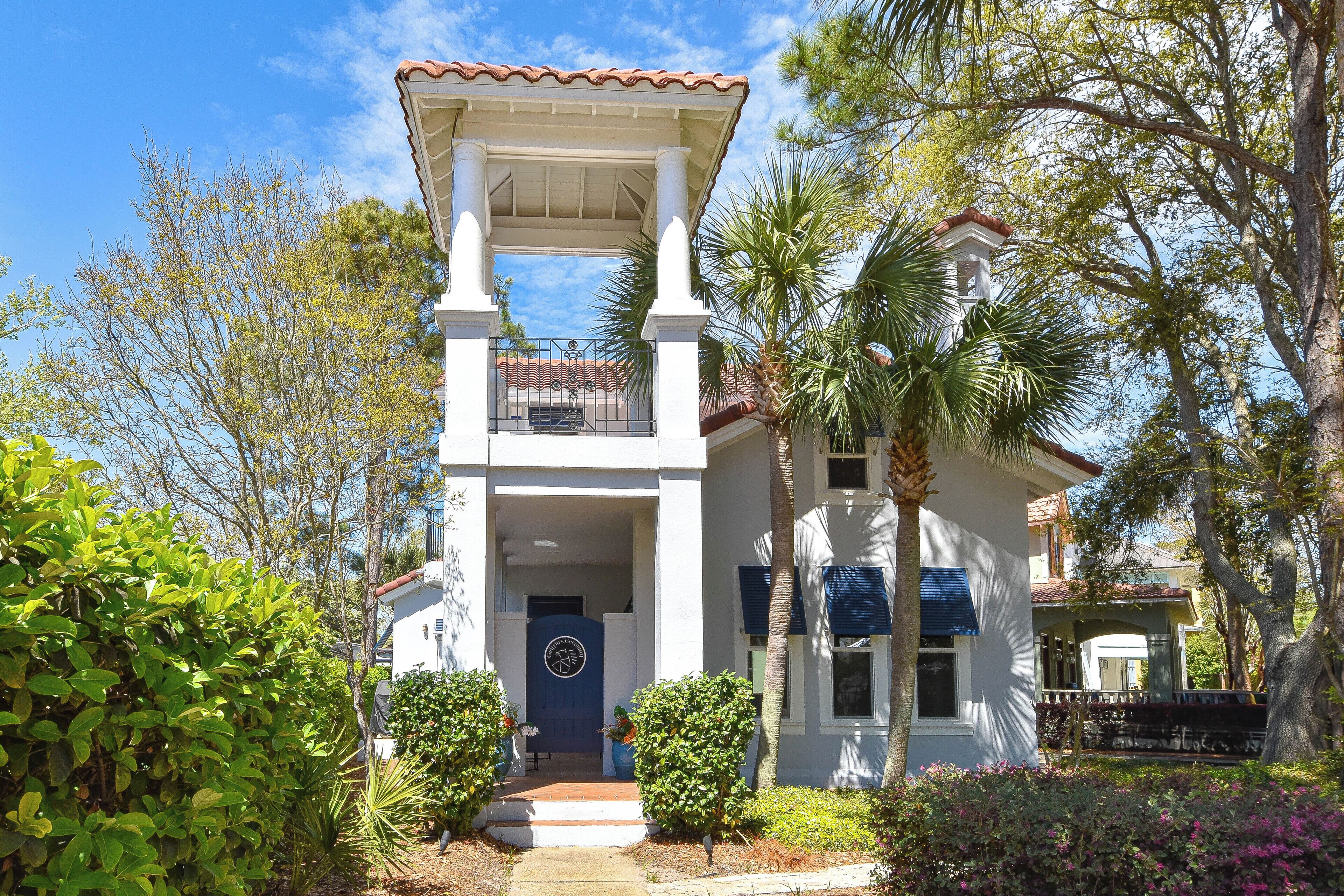 A two-story house with a white facade, a blue door, and a balcony.