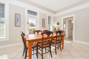 Un comedor con una mesa y sillas de madera, obras de arte en las paredes y vistas al exterior a través de las ventanas.